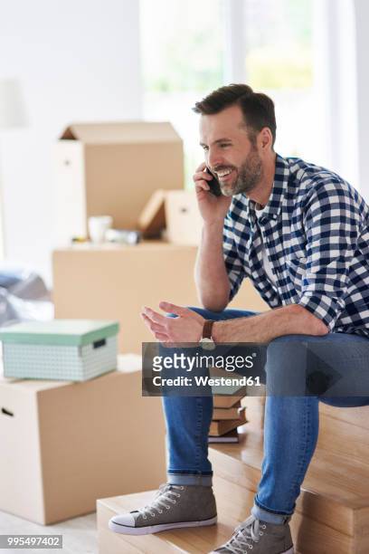 smiling man moving into new flat talking on cell phone - box white flat stock-fotos und bilder