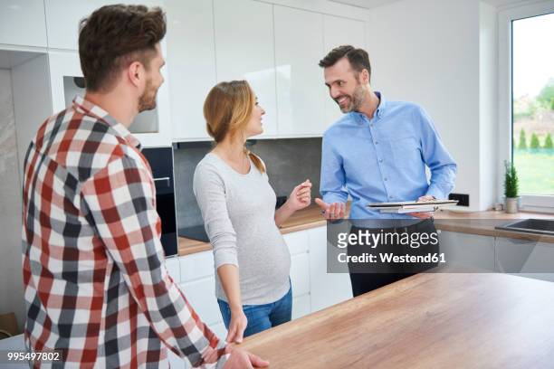 couple and real estate agent talking in kitchen of new apartment - ethnic millennial real estate stockfoto's en -beelden