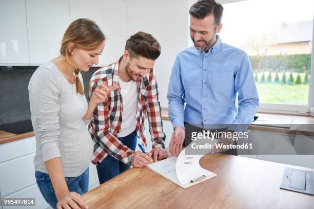 couple with real estate agent signing contract in kitchen of new apartment - ethnic millennial real estate stockfoto's en -beelden