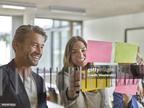 happy colleagues discussing with sticky notes at glass pane - coworkers having fun stock-fotos und bilder