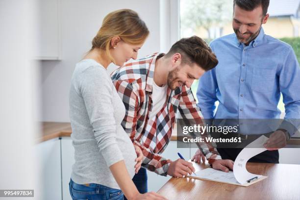 couple with real estate agent signing contract in kitchen of new apartment - friendly salesman fotografías e imágenes de stock