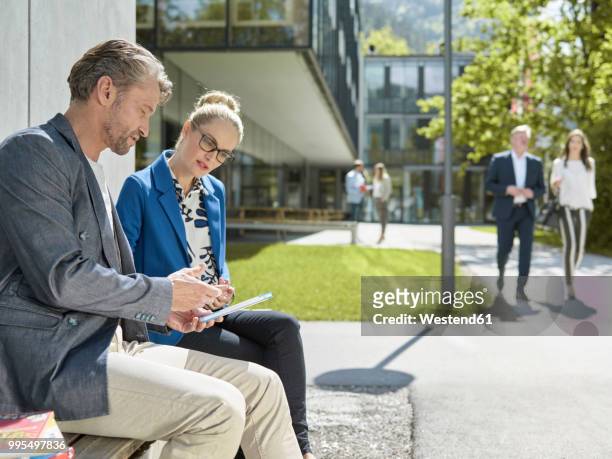 colleagues with tablet sitting on bench outside office building - bank meeting stock-fotos und bilder