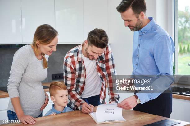 family with real estate agent signing contract in kitchen of new apartment - ethnic millennial real estate stockfoto's en -beelden
