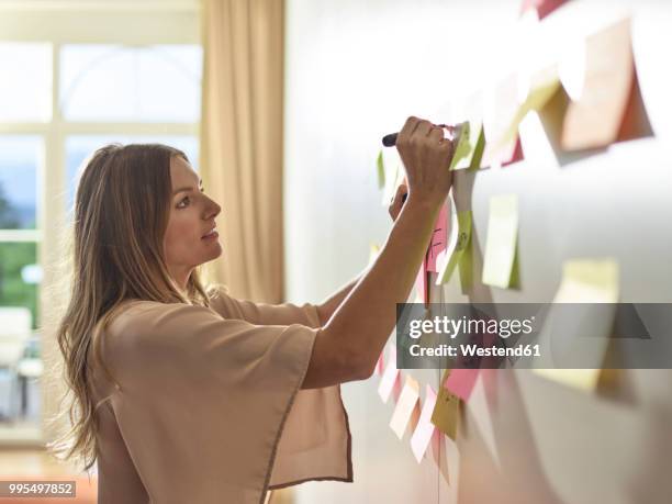 woman writing on sticky note at the wall - österreich durchblick stock-fotos und bilder