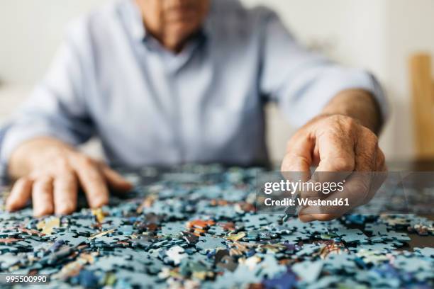 senior man doing a jigsaw - rompicapo foto e immagini stock