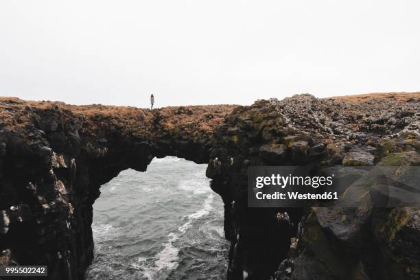 iceland, arnarstapi, woman standing on rock arch - arnarstapi stock-fotos und bilder