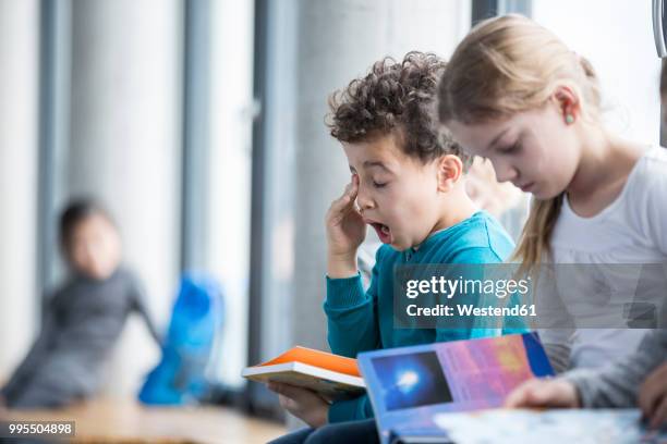tired schoolboy with book in school - kid rubbing eyes stock pictures, royalty-free photos & images