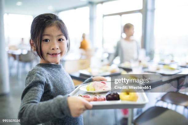 portrait of smiling schoolgirl carrying tray in school canteen - kantine stock-fotos und bilder