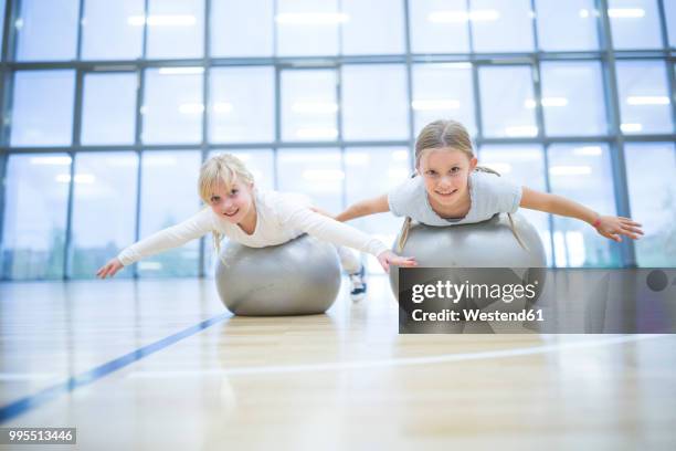 portrait of smiling schoolgirls balancing on gym balls in gym class - gymnastikball stock-fotos und bilder