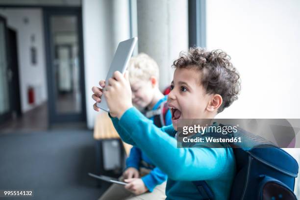 happy schoolboy holding up tablet on corridor in school - school tablet stock-fotos und bilder