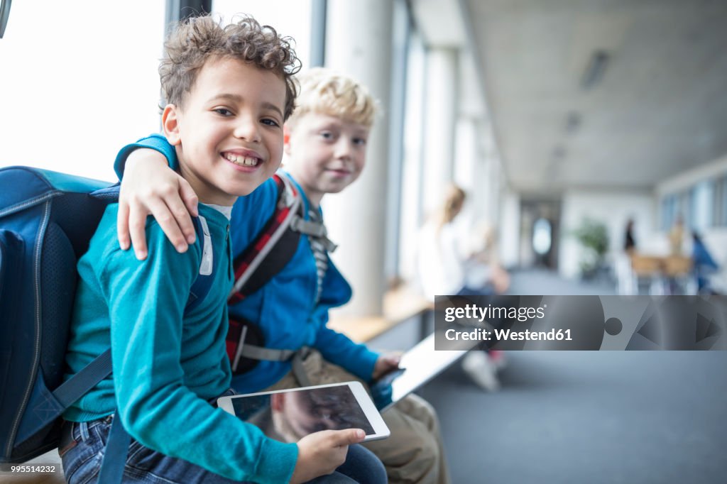 Portrait of two smiling schoolgboys with tablet embracing