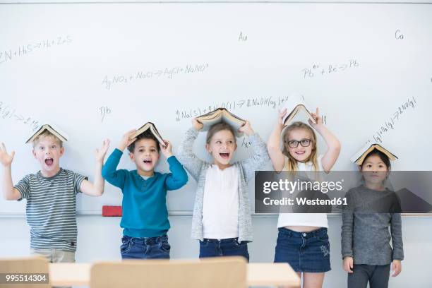 happy pupils with books above their heads standing at whiteboard with formulas in class - fun experience stock pictures, royalty-free photos & images