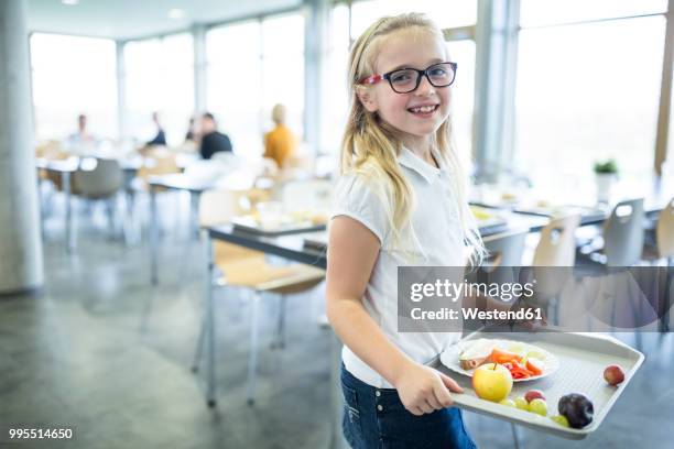 portrait of smiling schoolgirl carrying tray in school canteen - cafeteria foto e immagini stock