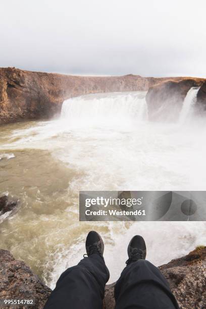 iceland, legs of a man sitting at godafoss waterfall - northeast iceland stockfoto's en -beelden