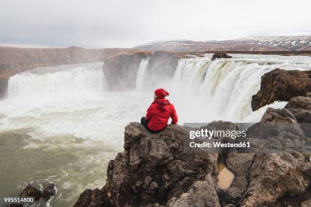 iceland, man sitting at godafoss waterfall - northeast iceland stockfoto's en -beelden