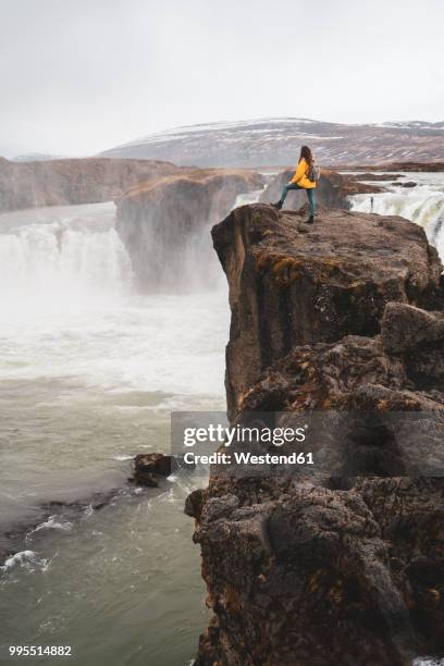 iceland, woman standing at godafoss waterfall - northeast iceland stockfoto's en -beelden