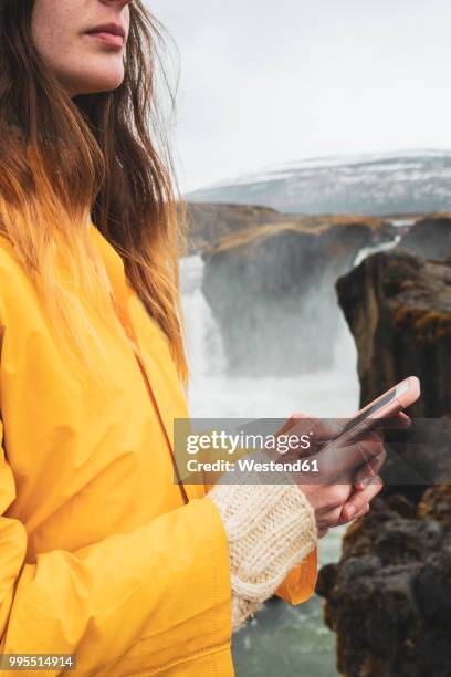 iceland, woman with cell phone at godafoss waterfall - northeast iceland stockfoto's en -beelden