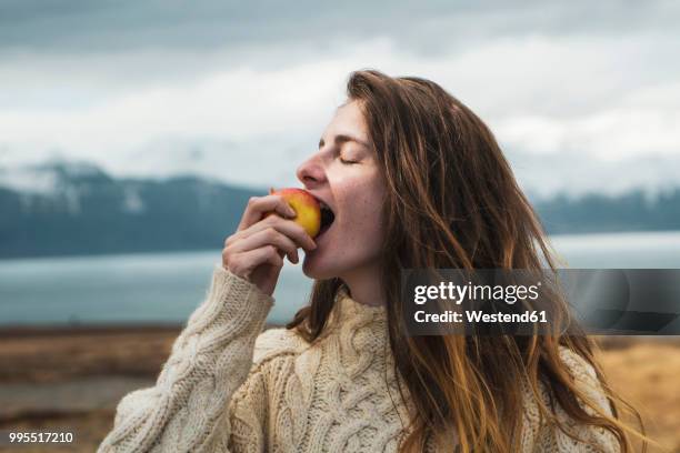 iceland, woman eating an apple at lakeside - nordic food stock-fotos und bilder