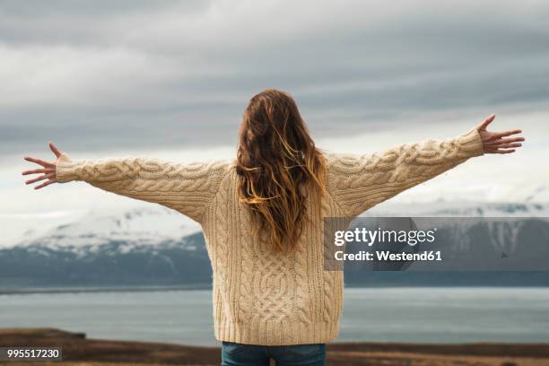 iceland, woman standing at lakeside with outstretched arms - mujer de espaldas en paisaje fotografías e imágenes de stock