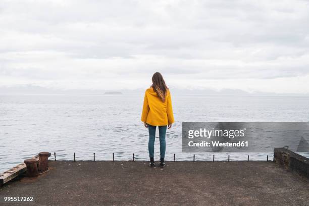 iceland, woman standing at the sea - abrigo amarillo fotografías e imágenes de stock