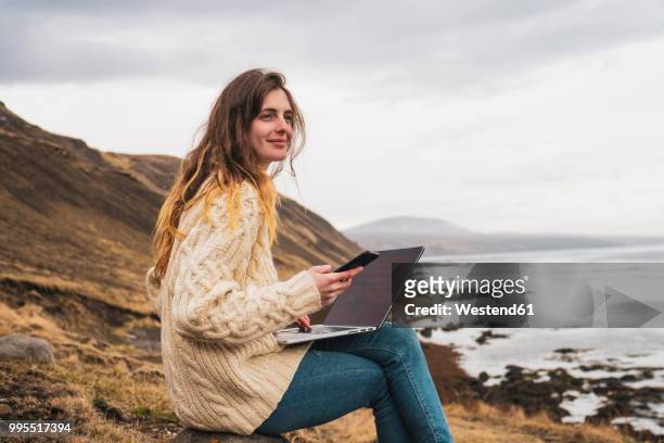 iceland, woman using laptop and cell phone at the coast - iceland landscape stock-fotos und bilder