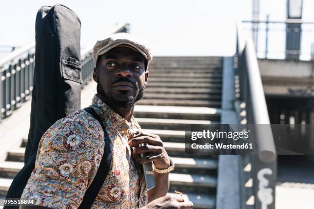 young man walking in the city, carrying guitar case - guitar case fotografías e imágenes de stock