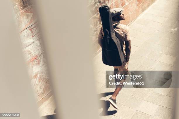 young man walking in the city, carrying guitar case - guitar case fotografías e imágenes de stock