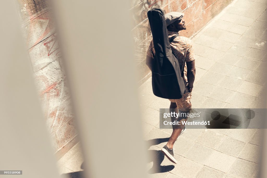 Young man walking in the city, carrying guitar case