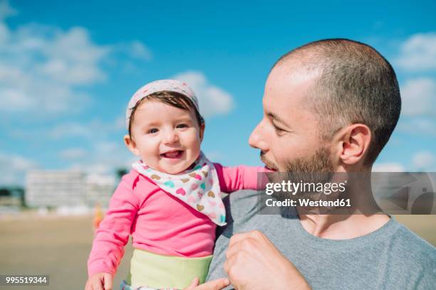 france, la baule, portrait of smiling baby girl on father's arms on the beach - la baule stock pictures, royalty-free photos & images