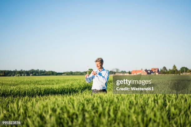 businessman standing in grain field, holding miniature wind wheel - guy standing in field stock pictures, royalty-free photos & images