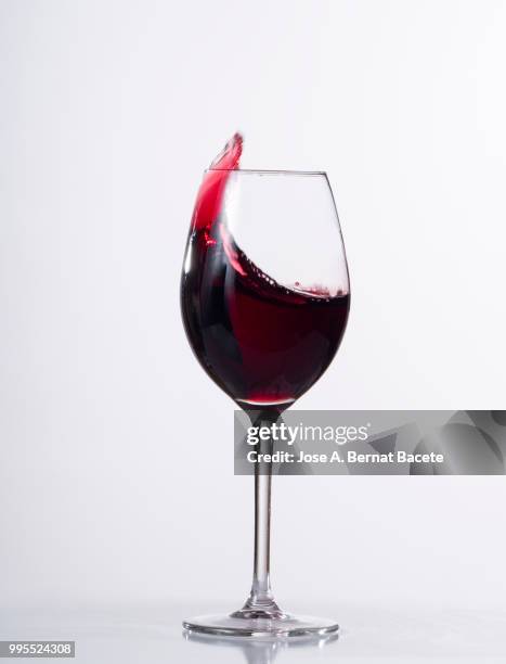 red wine splashing in glass in front of white background - kurzzeitfotografie stock-fotos und bilder