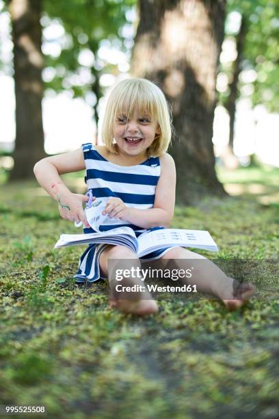 portrait of laughing little girl with painted face sitting on ground in nature - cute girl toddler stock-fotos und bilder