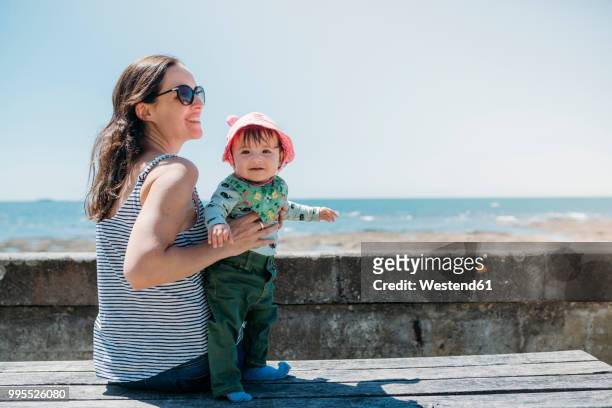 france, content mother and baby girl on a bench at beach promenade - atlantikküste frankreich stock-fotos und bilder