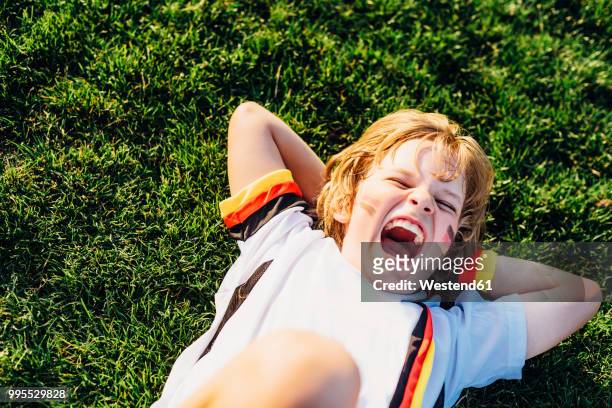 boy in german soccer shirt lying on grass, laughimg - german blonde fotografías e imágenes de stock