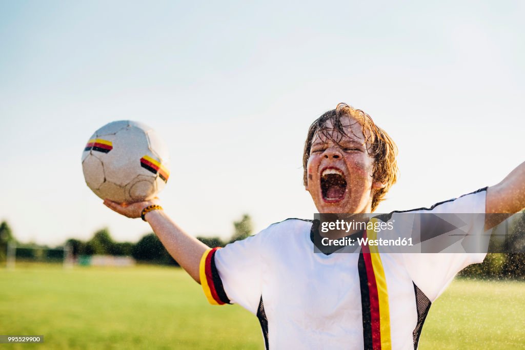Boy wearing German soccer shirt screaming for joy, standing in water splashes