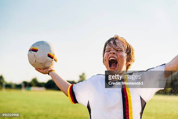 boy wearing german soccer shirt screaming for joy, standing in water splashes - fußball spielball stock-fotos und bilder