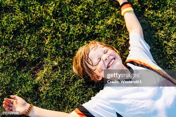 boy in german soccer shirt lying on grass, laughimg - germany soccer stock-fotos und bilder