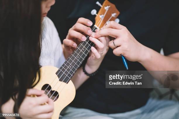 einen asiatischen chinesischen mann lehre eine asiatische chinesische frauen auf ukulele im wohnzimmer - ukulele stock-fotos und bilder