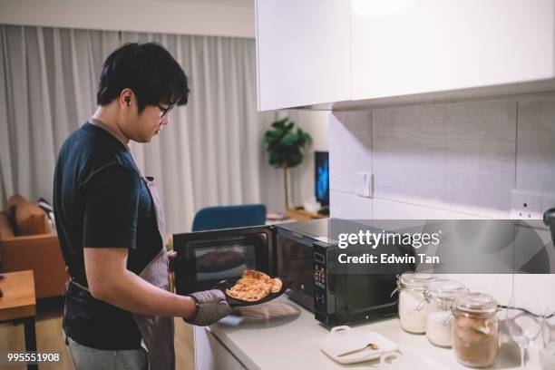 un homme chinois asiatique prenant une pizza de micro-ondes dans la cuisine avec un gant - microwave photos et images de collection