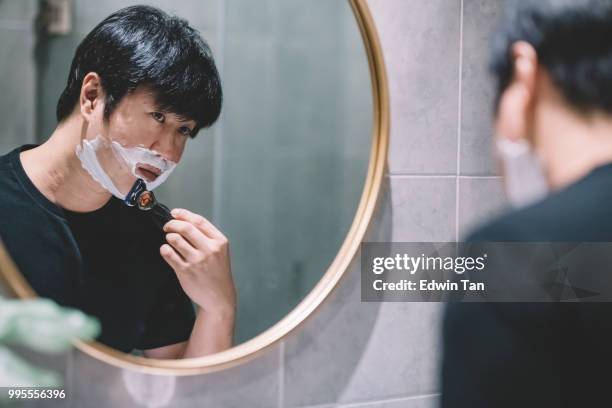 an asian chinese man shaving in the washroom in front of the mirror - man shaving foam stock pictures, royalty-free photos & images