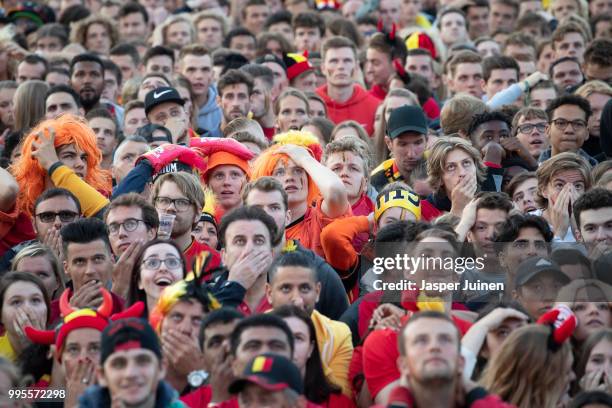 Belgian football fans react as France scores the opening goal while watching the World Cup Semi Final match between France and Belgium at a fan...