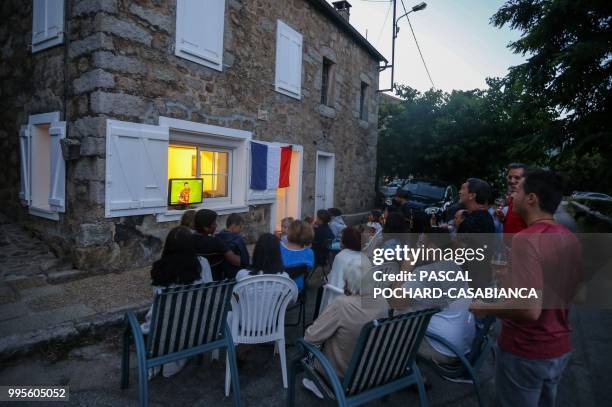 Residents sit outside as they watch a television in the village of Marato in Cognocoli-Monticchi on July 10 showing the 2018 semi-final Russia World...