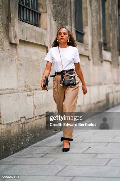 Guest wears a white t-shirt, a black leather bag, beige pants , outside Givenchy, during Paris Fashion Week Haute Couture Fall Winter 2018/2019, on...