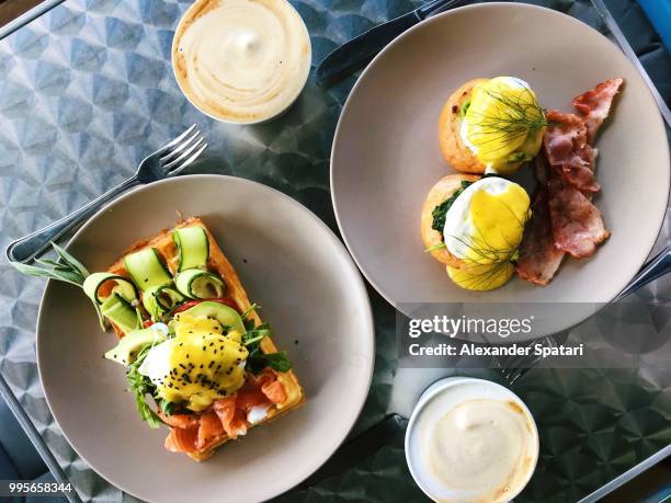 directly above view of brunch in a cafe with eggs benedict, waffle, salmon, avocado and coffee - eggs benedict stock pictures, royalty-free photos & images