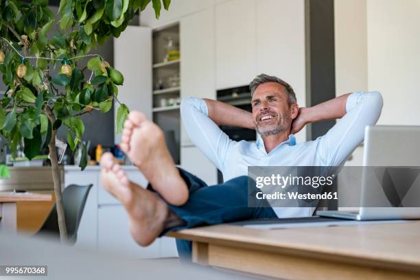 smiling mature man relaxing at home with laptop on table - at a glance foto e immagini stock