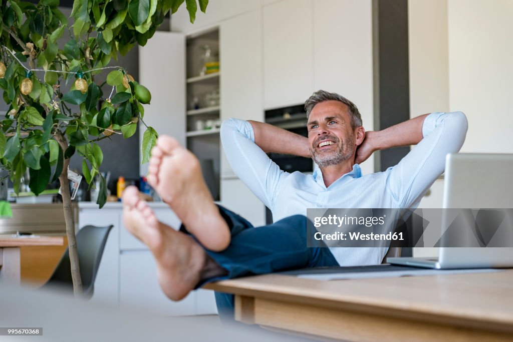 Smiling mature man relaxing at home with laptop on table