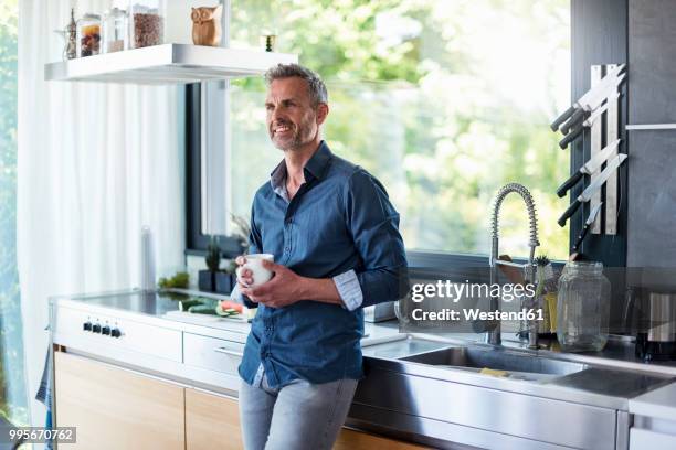 smiling mature man at home in kitchen with cup of coffee - kitchen coffee home stock-fotos und bilder