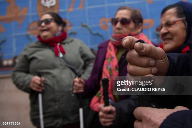 Blind people take a tour of a circuit of mural paintings which include tactile plates, in Santiago, on July 10, 2018. - 'Manos a la pared' , the...
