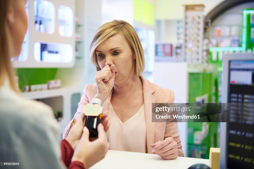 Pharmacist selling cough syrup to woman in pharmacy