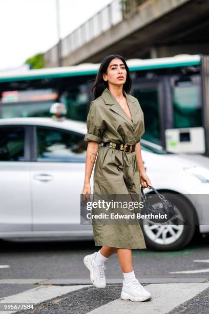 Guest wears a green khaki trench coat dress, a black leather belt with golden part, white sneakers shoes , outside Vetements, during Paris Fashion...